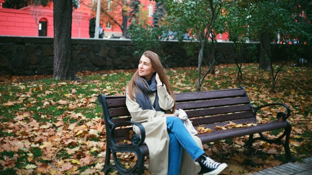 woman in brown coat sitting on brown wooden bench