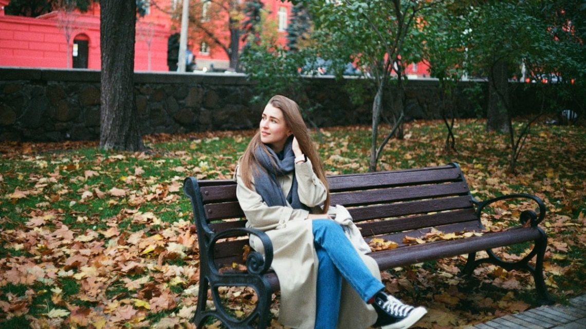 woman in brown coat sitting on brown wooden bench
