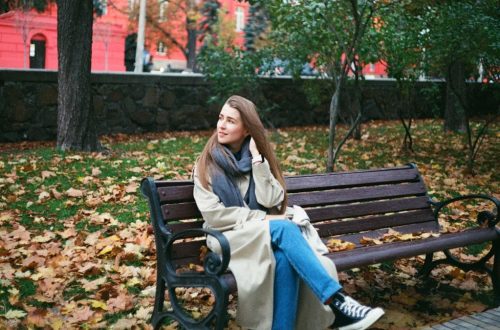 woman in brown coat sitting on brown wooden bench