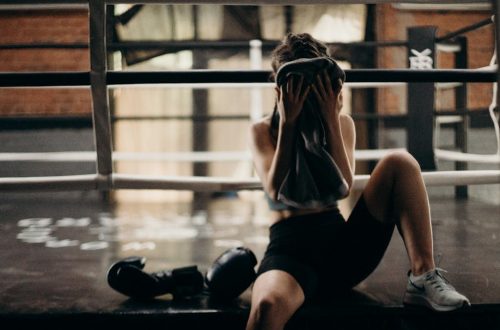 A female boxer sitting in a gym ring, resting and wiping sweat with a towel after a workout.