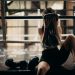 A female boxer sitting in a gym ring, resting and wiping sweat with a towel after a workout.